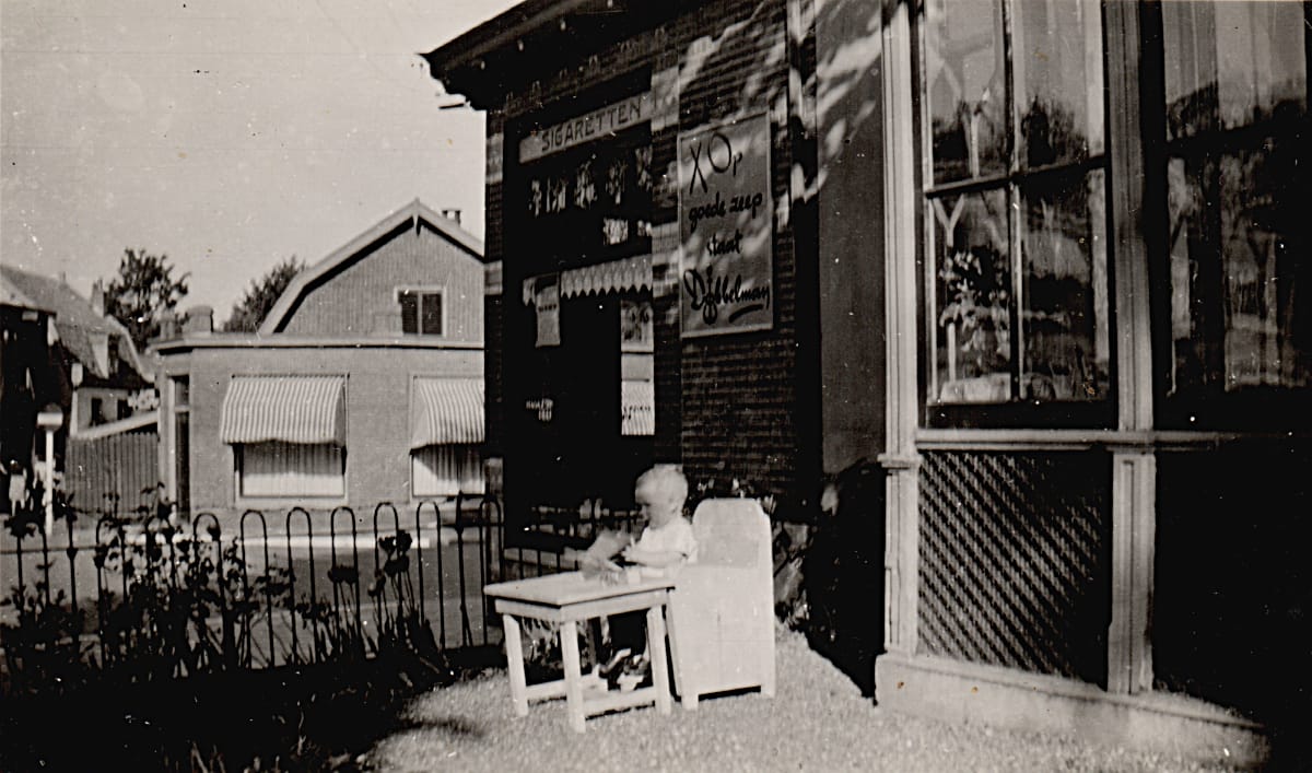 De sigarenwinkel van de heer Van Dam, met daarvoor een kind op een stoel
